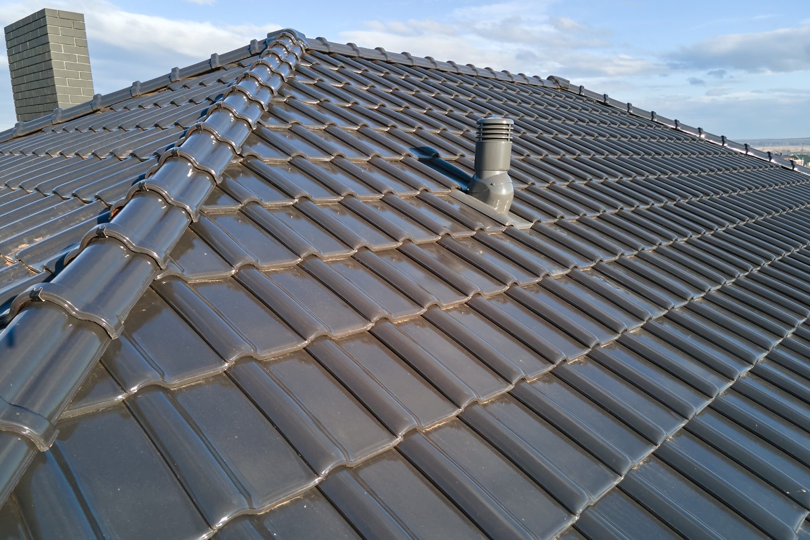 Closeup of ventilation pipe on house roof top covered with ceramic shingles. Tiled covering of building.